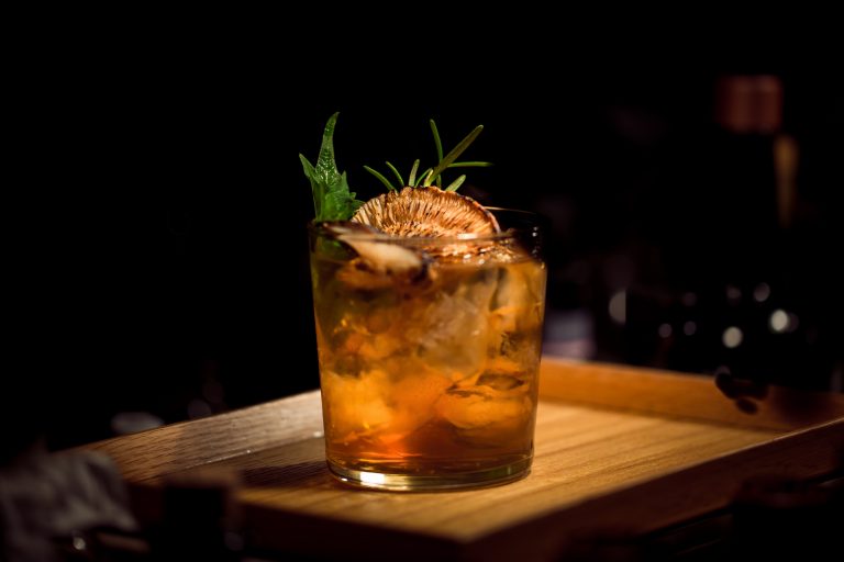 bourbon based cocktail with passionfruit garnish basthed in light on wooden board